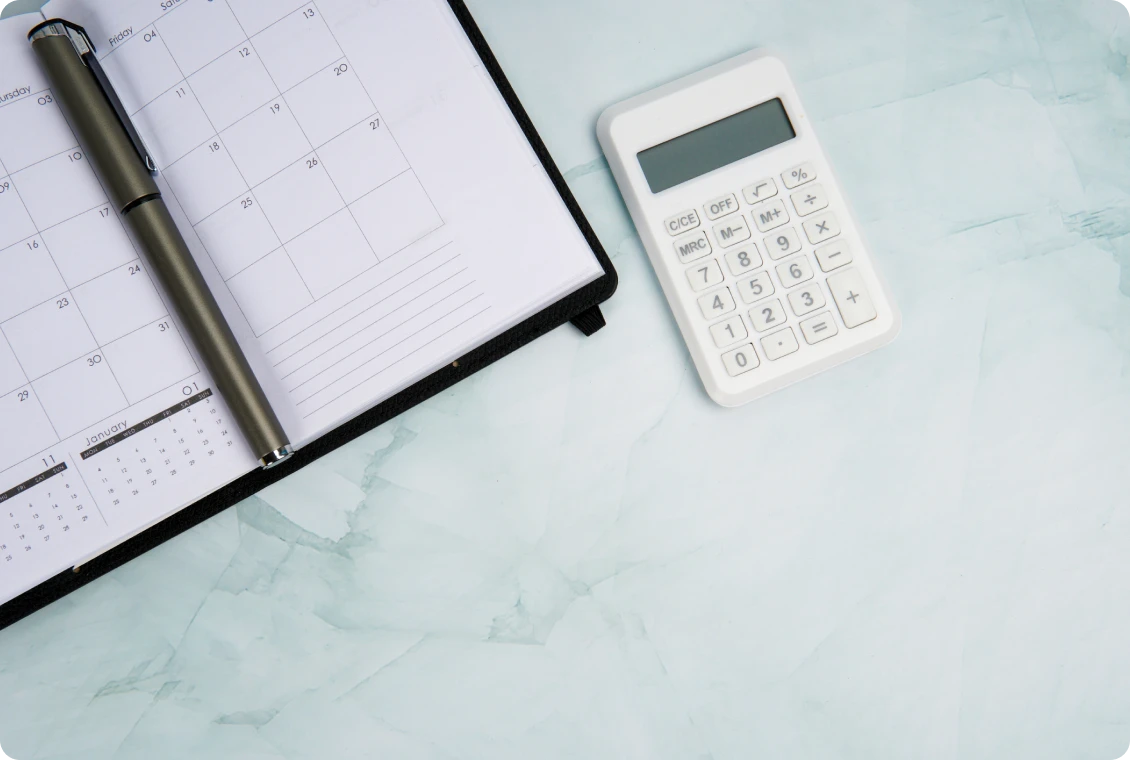 Planner, pen, and calculator on marble surface